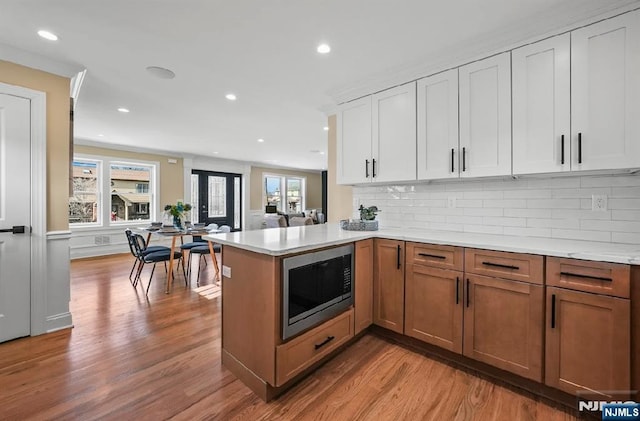 kitchen with built in microwave, tasteful backsplash, kitchen peninsula, light hardwood / wood-style floors, and white cabinets