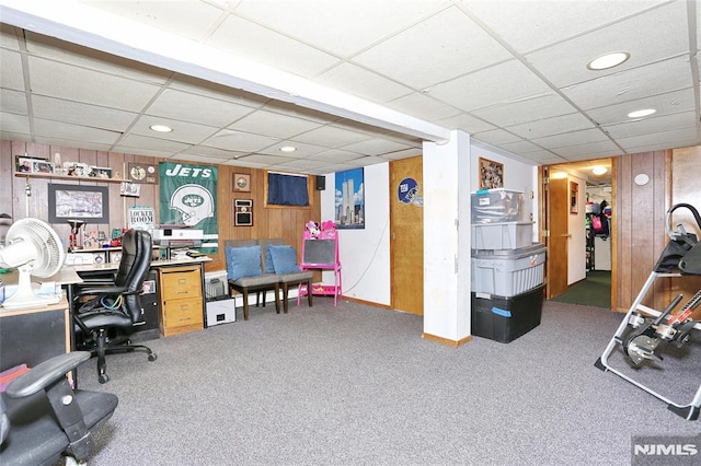 carpeted office space with a drop ceiling and wood walls