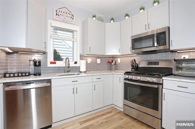 kitchen with sink, white cabinetry, stainless steel appliances, tasteful backsplash, and light hardwood / wood-style floors