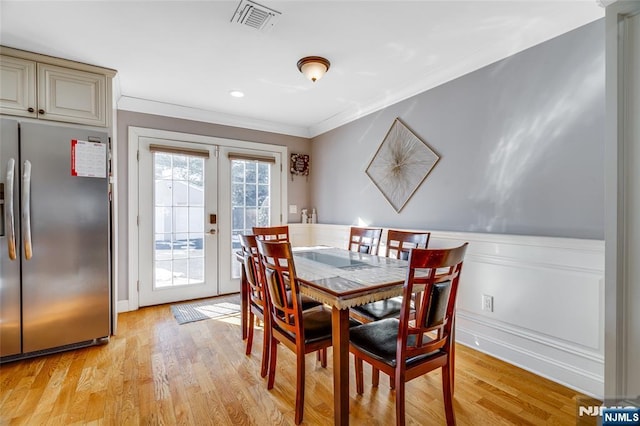 dining space featuring french doors, ornamental molding, and light wood-type flooring