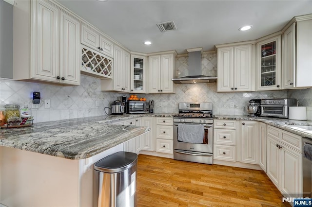 kitchen with wall chimney exhaust hood, stainless steel appliances, light hardwood / wood-style floors, and light stone counters