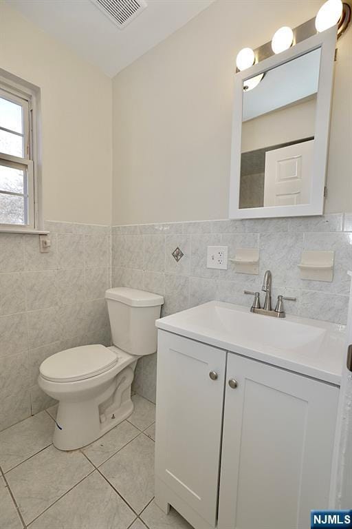 bathroom with tile patterned floors, vanity, toilet, and tile walls