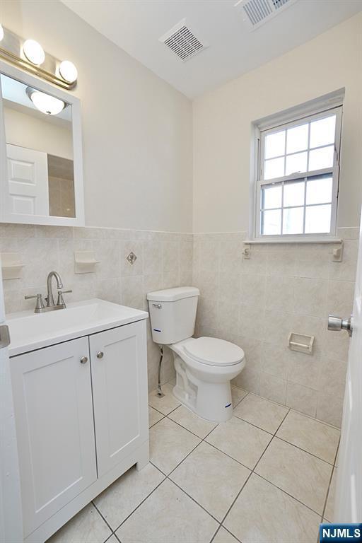 bathroom featuring vanity, toilet, tile patterned flooring, and tile walls