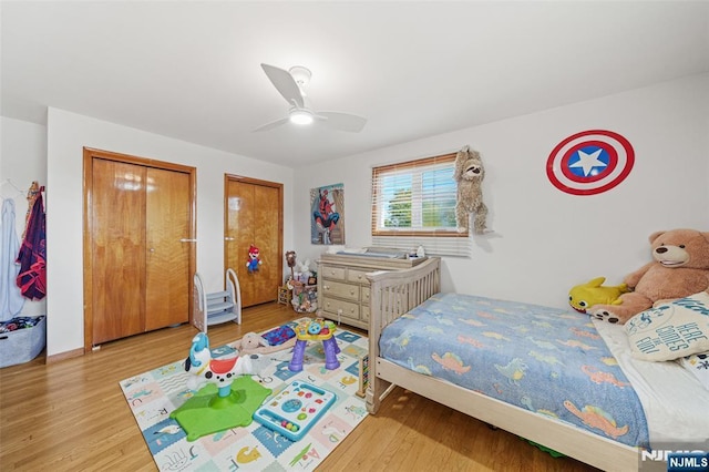 bedroom with two closets, light hardwood / wood-style floors, and ceiling fan