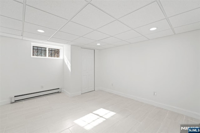 basement with a baseboard radiator and a drop ceiling