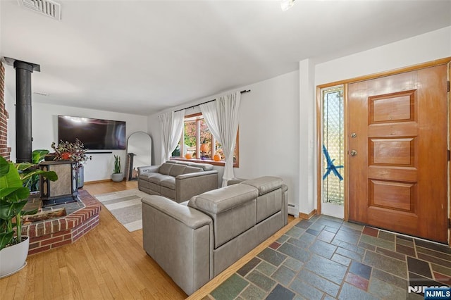 living room with a baseboard heating unit, hardwood / wood-style flooring, and a wood stove