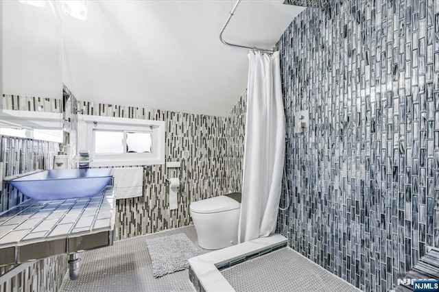 bathroom with vaulted ceiling, tile walls, toilet, tile patterned floors, and a shower with curtain