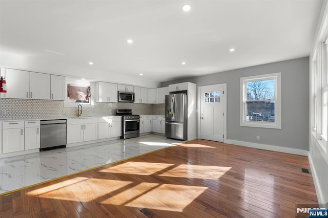 kitchen featuring sink, white cabinetry, backsplash, stainless steel appliances, and light hardwood / wood-style floors