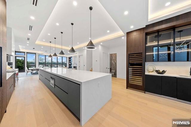 kitchen featuring a large island, wine cooler, light hardwood / wood-style floors, decorative light fixtures, and a raised ceiling