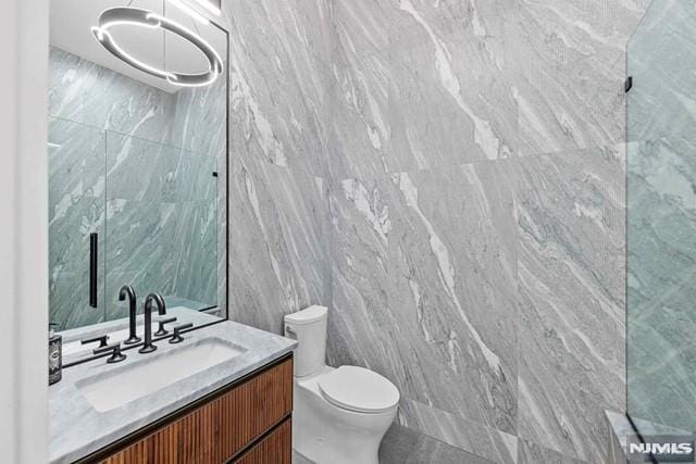 bathroom with vanity, tile walls, and toilet