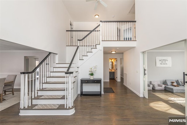 stairs with crown molding, a towering ceiling, and wood-type flooring