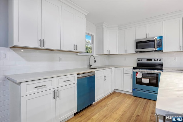 kitchen featuring appliances with stainless steel finishes, white cabinetry, sink, decorative backsplash, and light hardwood / wood-style flooring