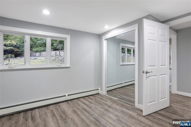 unfurnished room featuring a baseboard heating unit, plenty of natural light, and light wood-type flooring