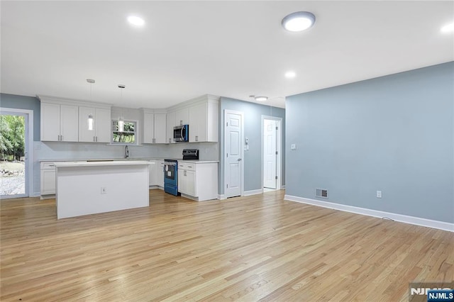 kitchen with a kitchen island, appliances with stainless steel finishes, pendant lighting, white cabinets, and light wood-type flooring