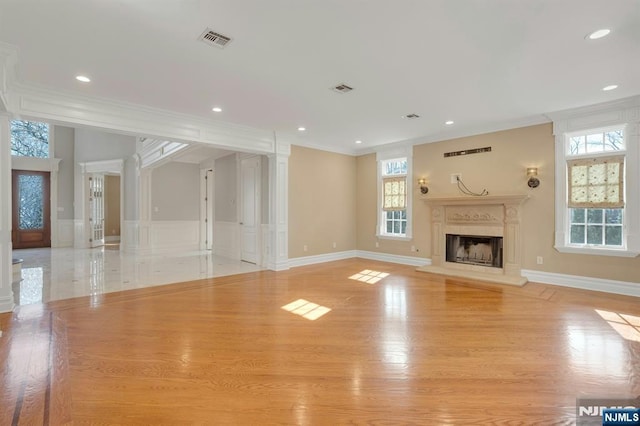 unfurnished living room with crown molding, a wealth of natural light, and light hardwood / wood-style floors