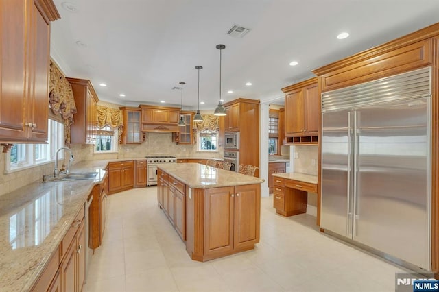 kitchen featuring sink, built in appliances, a center island, hanging light fixtures, and light stone countertops