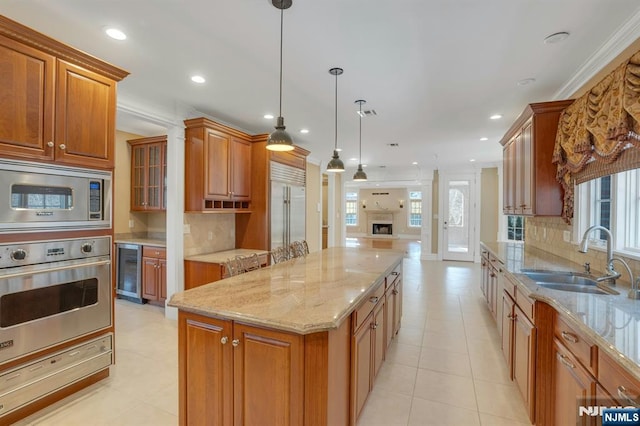 kitchen with sink, hanging light fixtures, a center island, built in appliances, and beverage cooler