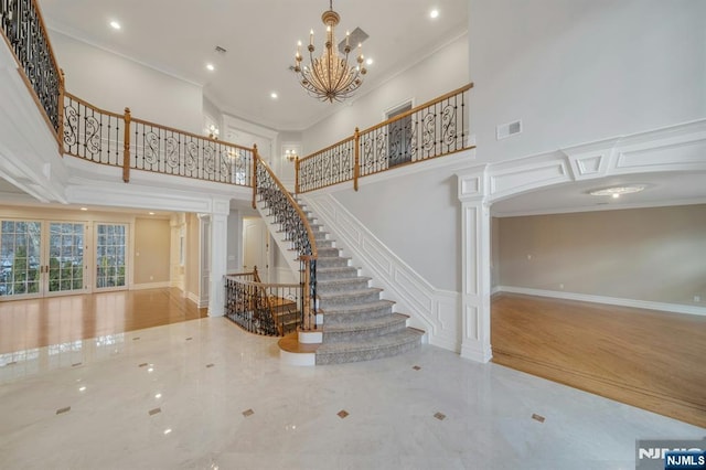 stairs featuring a towering ceiling, ornamental molding, decorative columns, and a notable chandelier