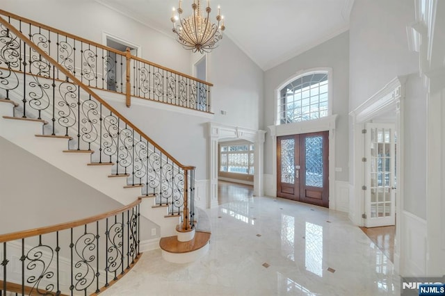 foyer with crown molding, a towering ceiling, a chandelier, and french doors