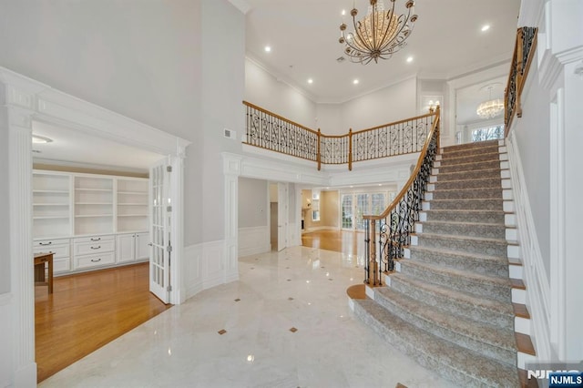 entryway featuring crown molding, a towering ceiling, and an inviting chandelier