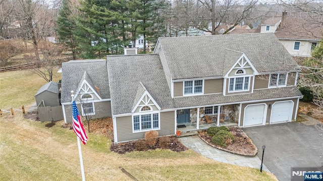 view of front facade featuring a chimney, covered porch, a front yard, fence, and driveway