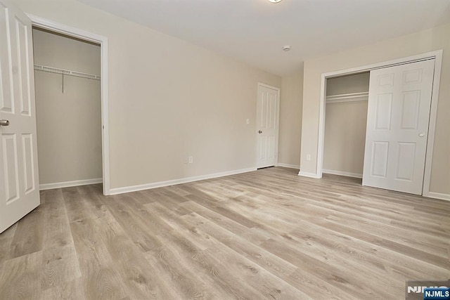 unfurnished bedroom with two closets and light hardwood / wood-style floors