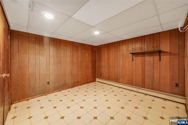 spare room featuring a drop ceiling, baseboard heating, and wood walls