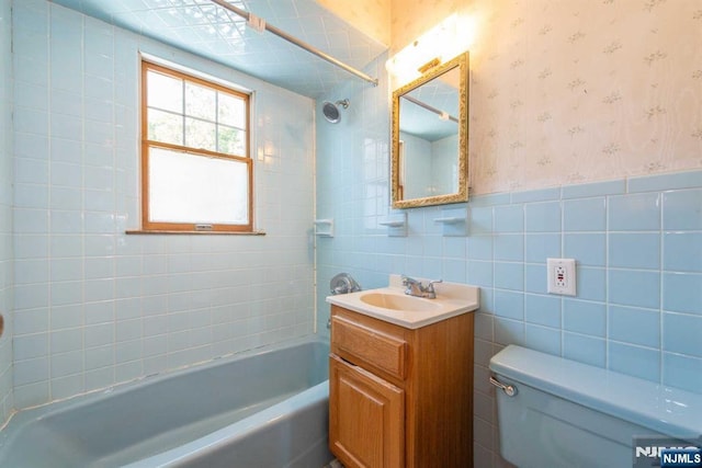 full bathroom with vanity, toilet, tiled shower / bath combo, and tile walls