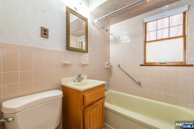 full bathroom featuring tiled shower / bath, vanity, toilet, and tile walls