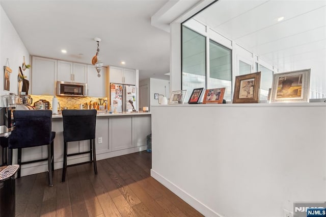 kitchen with white cabinetry, fridge, a kitchen breakfast bar, kitchen peninsula, and dark hardwood / wood-style floors