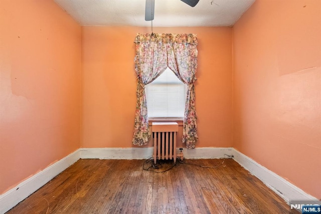 empty room featuring hardwood / wood-style flooring, radiator, and ceiling fan