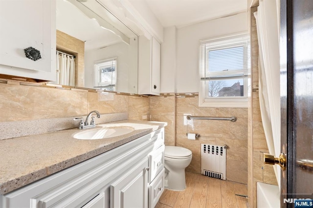 bathroom with radiator heating unit, tile walls, hardwood / wood-style flooring, vanity, and toilet