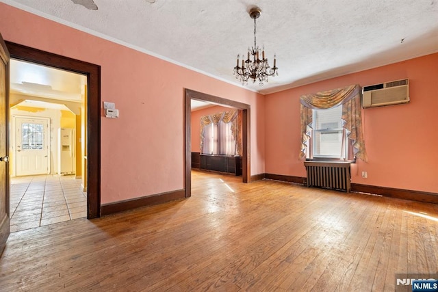 empty room featuring radiator, hardwood / wood-style floors, a textured ceiling, and an AC wall unit