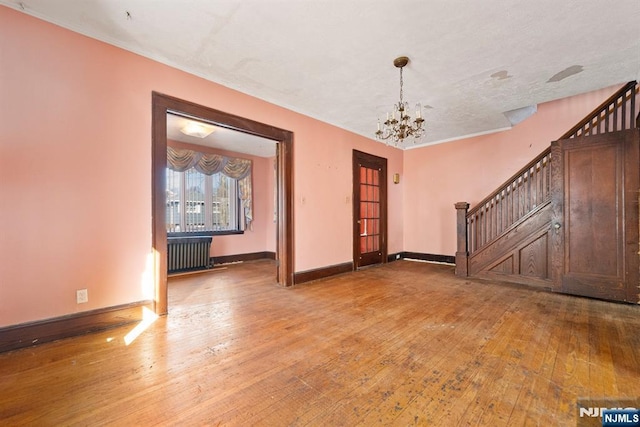 unfurnished room featuring hardwood / wood-style flooring, radiator, and an inviting chandelier