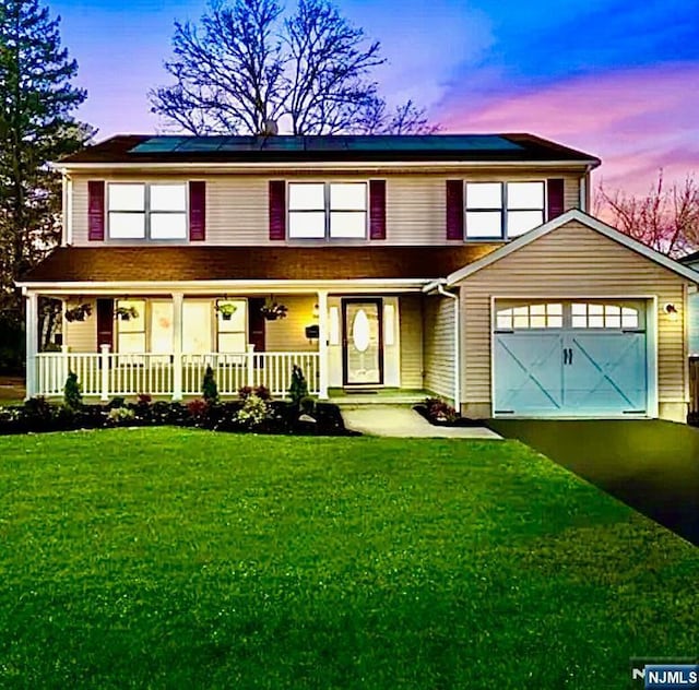 view of front of property featuring a garage, a yard, solar panels, and a porch