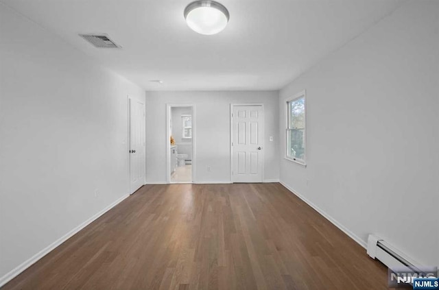 empty room with dark hardwood / wood-style floors and a baseboard heating unit