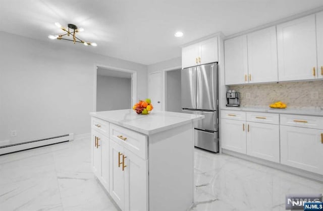 kitchen featuring stainless steel refrigerator, baseboard heating, a kitchen island, white cabinets, and backsplash