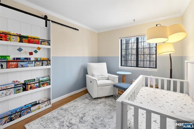 bedroom with crown molding, a barn door, light hardwood / wood-style flooring, and a crib