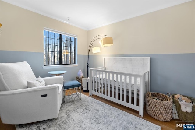 bedroom featuring ornamental molding, a nursery area, and hardwood / wood-style floors