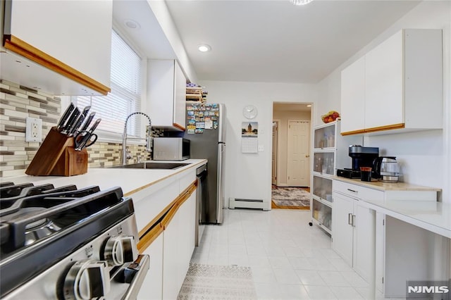 kitchen with sink, white cabinetry, tasteful backsplash, stainless steel range, and a baseboard heating unit