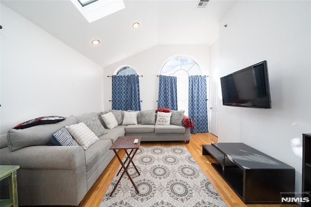 living room featuring vaulted ceiling with skylight and light hardwood / wood-style flooring