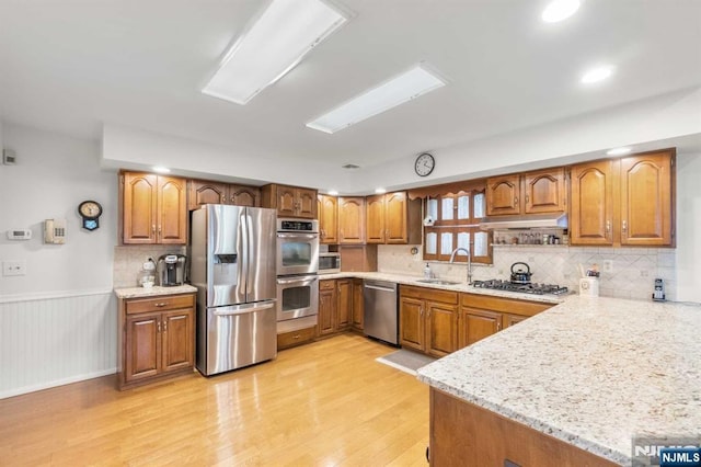 kitchen with appliances with stainless steel finishes, tasteful backsplash, sink, light stone countertops, and light wood-type flooring