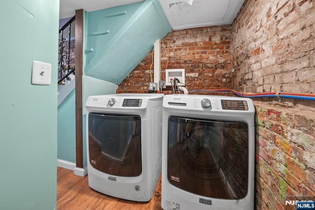 washroom featuring washing machine and clothes dryer, brick wall, and light wood-type flooring