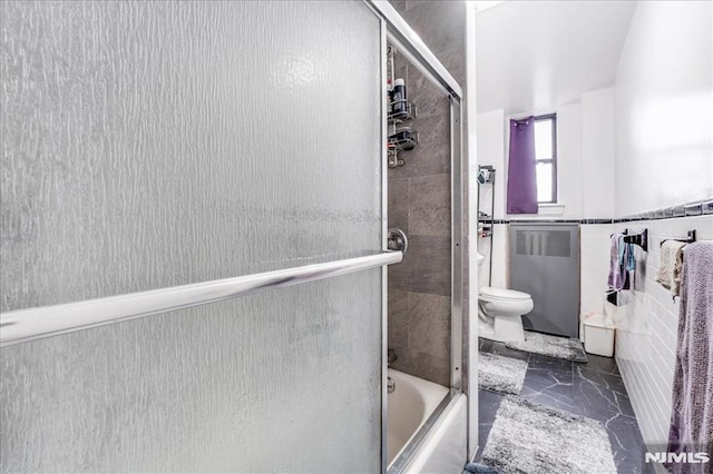 bathroom featuring marble finish floor, a wainscoted wall, radiator, toilet, and enclosed tub / shower combo