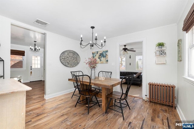 dining room with an inviting chandelier, radiator heating unit, ornamental molding, and wood-type flooring