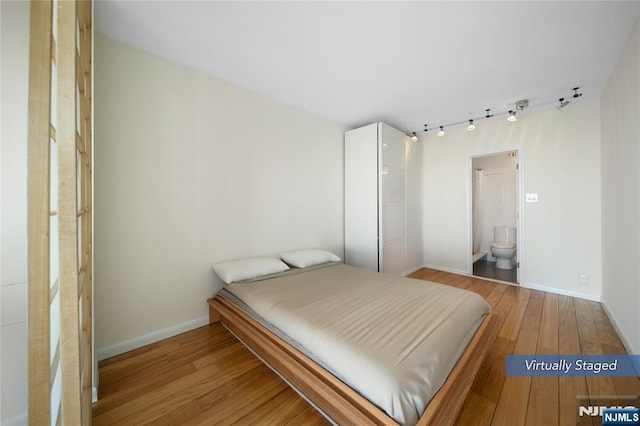 bedroom with hardwood / wood-style flooring, ensuite bath, baseboards, and rail lighting