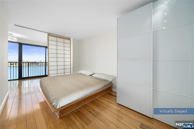 bedroom with access to outside, wood finished floors, and floor to ceiling windows