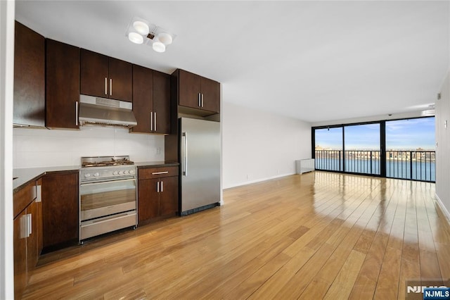 kitchen with light wood-style floors, appliances with stainless steel finishes, open floor plan, under cabinet range hood, and floor to ceiling windows