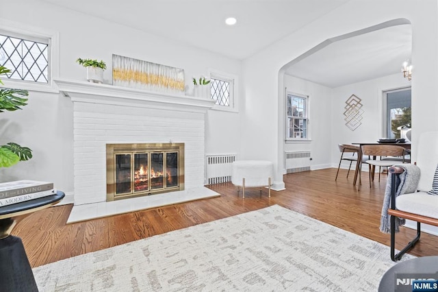 sitting room featuring hardwood / wood-style flooring, radiator heating unit, and a brick fireplace