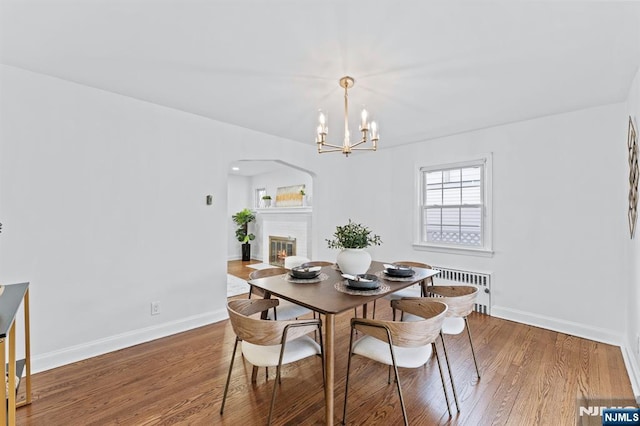 dining room featuring hardwood / wood-style flooring, radiator heating unit, a notable chandelier, and a fireplace